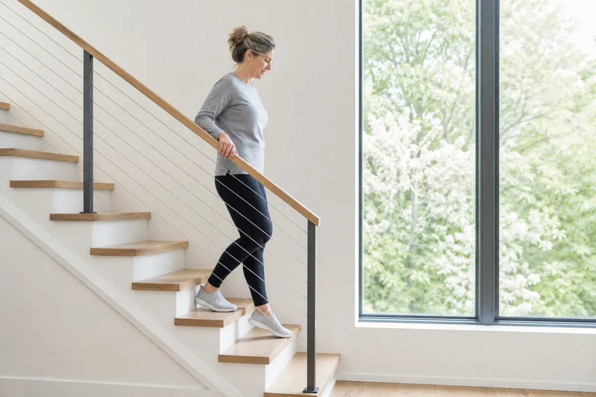 A woman in her forties descending a bright stairwell with controlled foot placement